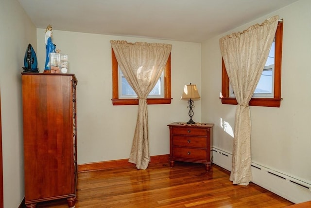 sitting room with a baseboard heating unit, wood finished floors, and baseboards