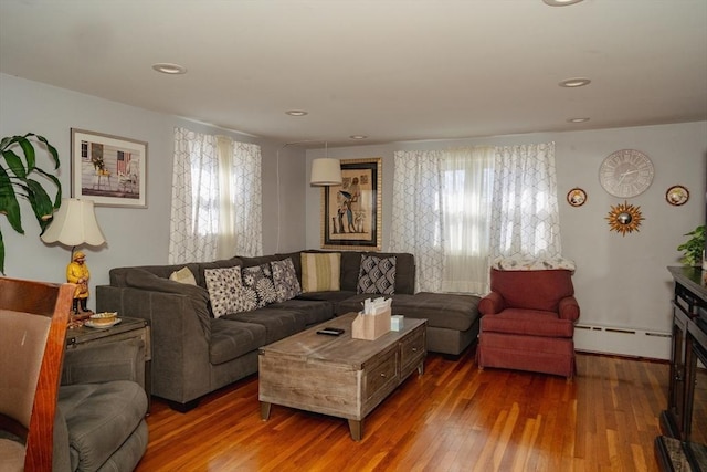 living room with a baseboard heating unit, a glass covered fireplace, wood finished floors, and recessed lighting