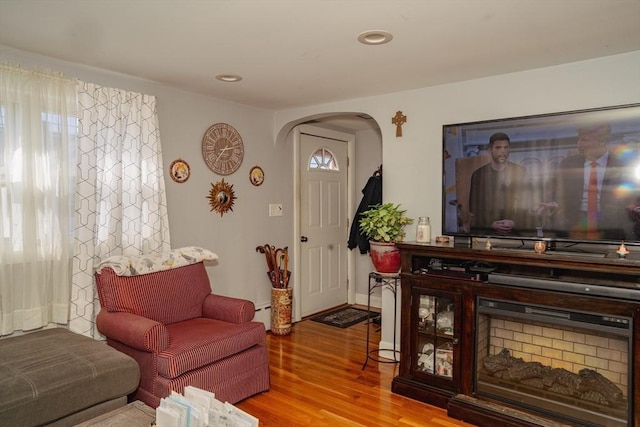 living area featuring arched walkways, a baseboard radiator, recessed lighting, wood finished floors, and baseboards