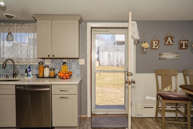 kitchen with wood finished floors, light countertops, baseboard heating, stainless steel dishwasher, and a sink