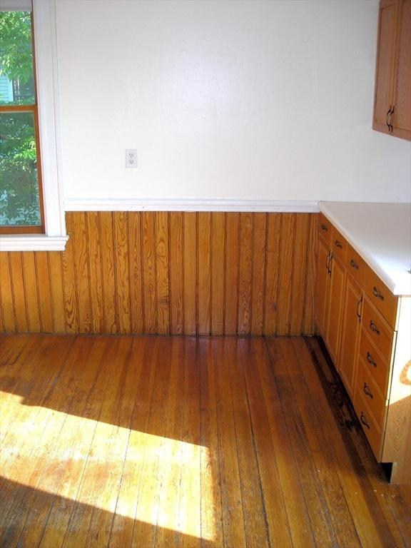 unfurnished dining area featuring wood-type flooring, a wainscoted wall, and plenty of natural light