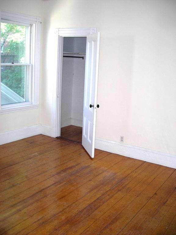 unfurnished bedroom featuring wood-type flooring, baseboards, and a closet