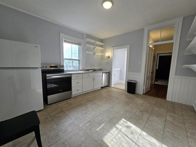 kitchen featuring appliances with stainless steel finishes, a wainscoted wall, white cabinets, a sink, and open shelves