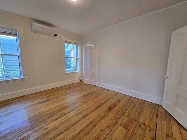 empty room featuring light wood-style flooring, a wall unit AC, baseboards, and crown molding