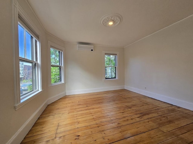 empty room with a wall mounted AC, plenty of natural light, light wood-type flooring, and baseboards
