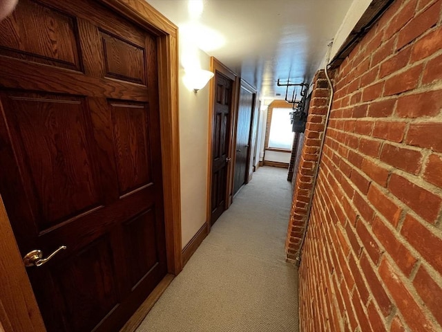 hallway with light carpet, brick wall, and baseboards