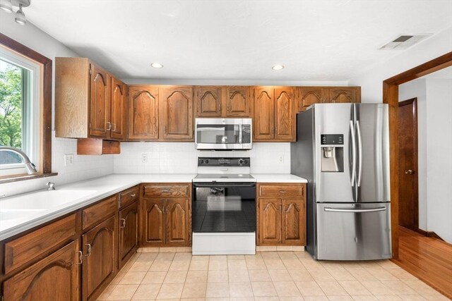 27 Woodland St, Natick, MA 01760 - kitchen featuring appliances with stainless steel finishes, a sink, light countertops, decorative backsplash, and brown cabinetry