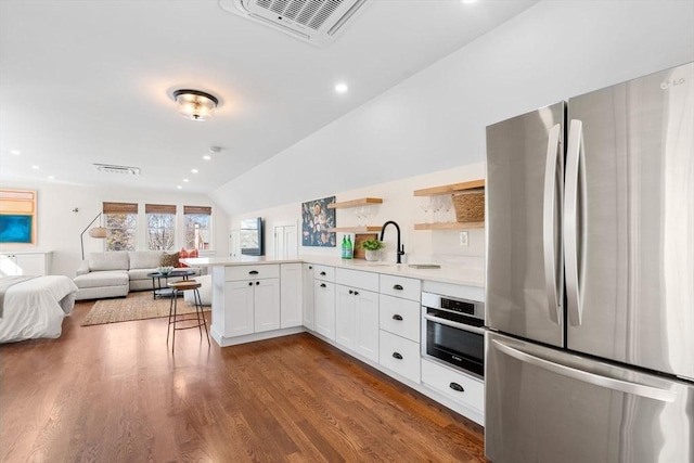 kitchen featuring visible vents, open floor plan, wood finished floors, appliances with stainless steel finishes, and vaulted ceiling