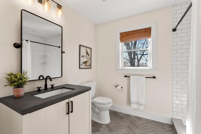 bathroom with vanity, toilet, baseboards, and a tile shower