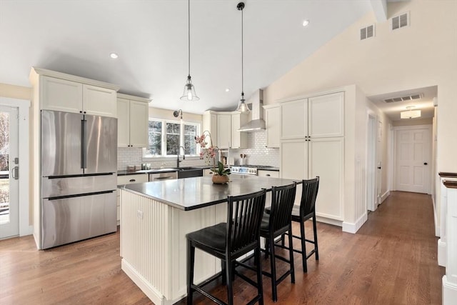 kitchen featuring visible vents, wall chimney exhaust hood, freestanding refrigerator, and wood finished floors