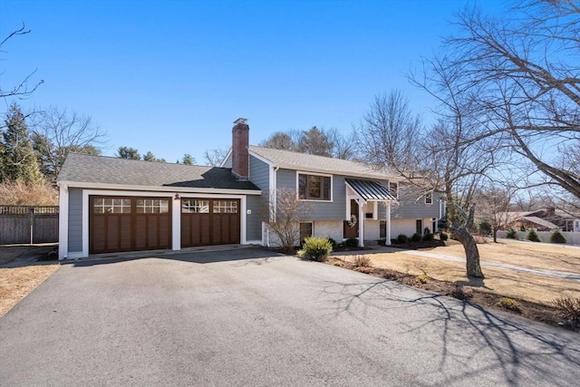 raised ranch featuring driveway, a chimney, an attached garage, and fence