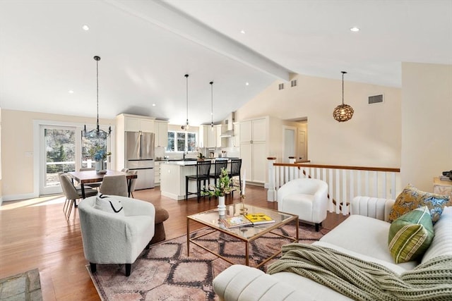 living room featuring beam ceiling, visible vents, a wealth of natural light, and light wood-style floors