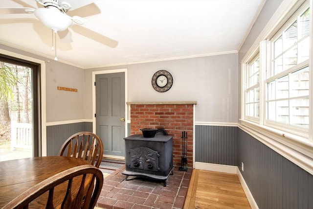 dining space featuring a wainscoted wall, crown molding, a wood stove, and wood finished floors