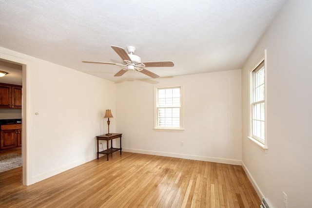 spare room featuring a ceiling fan, baseboards, light wood-type flooring, and a textured ceiling