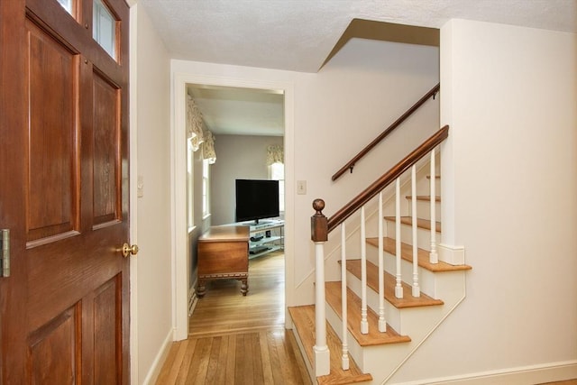 entryway with stairway, baseboards, light wood-type flooring, and a textured ceiling