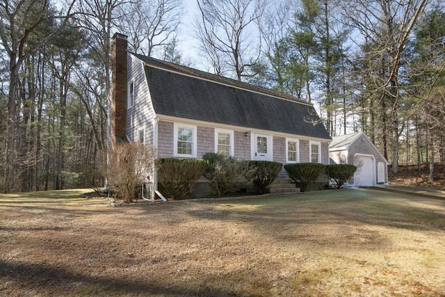 colonial inspired home with roof with shingles, a gambrel roof, a chimney, an outdoor structure, and a front lawn