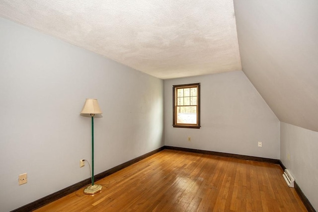 additional living space with hardwood / wood-style flooring, vaulted ceiling, baseboards, and a textured ceiling