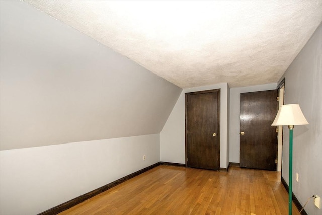 bonus room with baseboards, a textured ceiling, hardwood / wood-style floors, and vaulted ceiling