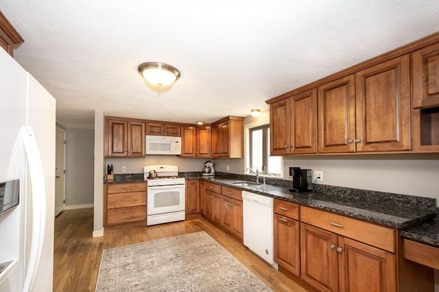 kitchen featuring dark stone counters, light wood-type flooring, brown cabinets, white appliances, and a sink