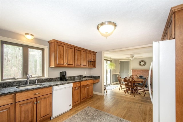 kitchen with white appliances, brown cabinets, dark stone counters, a sink, and light wood-type flooring