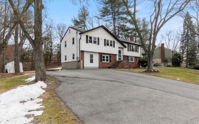 view of front facade featuring aphalt driveway, a chimney, a front lawn, and brick siding