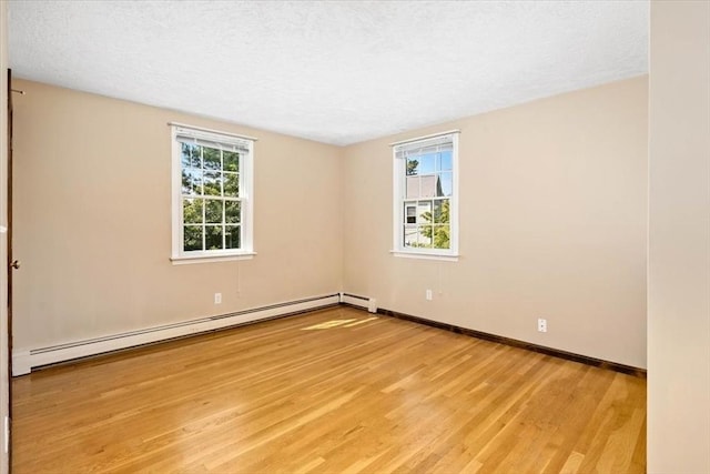 spare room featuring a wealth of natural light, a textured ceiling, baseboard heating, and light hardwood / wood-style floors