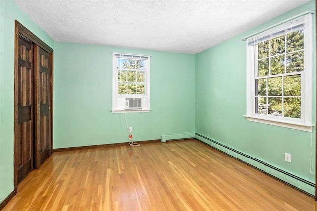 unfurnished room with a textured ceiling, baseboard heating, and light hardwood / wood-style floors