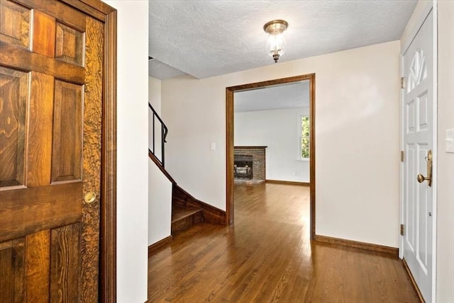 entryway featuring wood-type flooring, a brick fireplace, and a textured ceiling