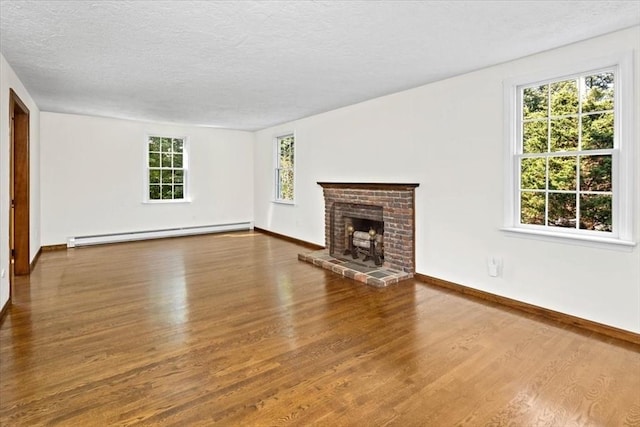 unfurnished living room with baseboard heating, wood-type flooring, a brick fireplace, and a textured ceiling