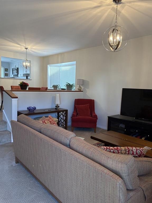 carpeted living area featuring stairs, baseboards, and a notable chandelier