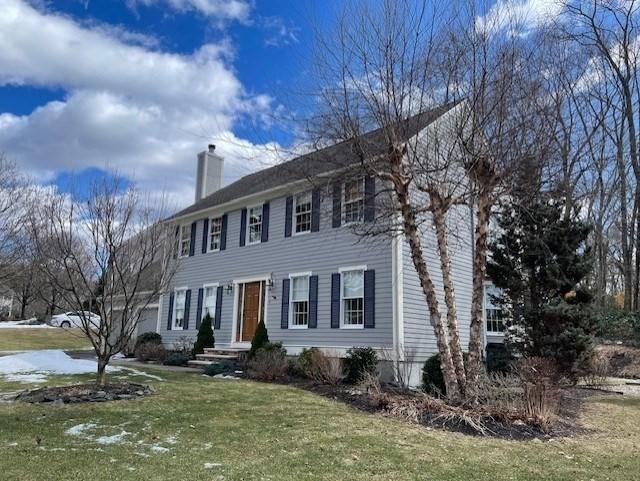 colonial inspired home with a garage, a front lawn, and a chimney