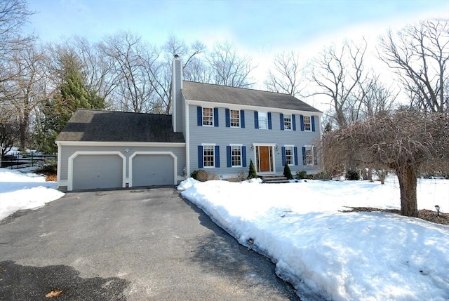 colonial inspired home with a garage, driveway, and a chimney