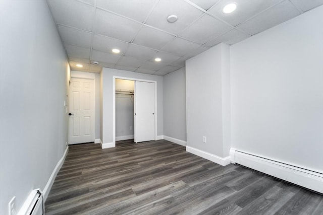 unfurnished bedroom featuring a baseboard heating unit, a drop ceiling, dark hardwood / wood-style floors, and a closet