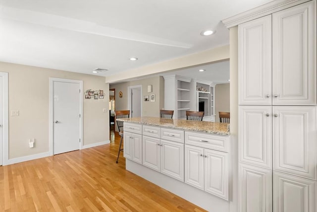 12 Shore Ave, Salem, MA 01970 - kitchen featuring light wood finished floors, a peninsula, light stone countertops, a kitchen breakfast bar, and recessed lighting