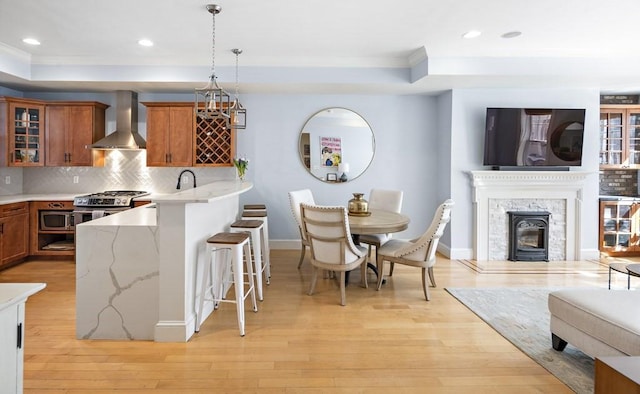 kitchen featuring a tray ceiling, wall chimney range hood, hanging light fixtures, and light hardwood / wood-style flooring