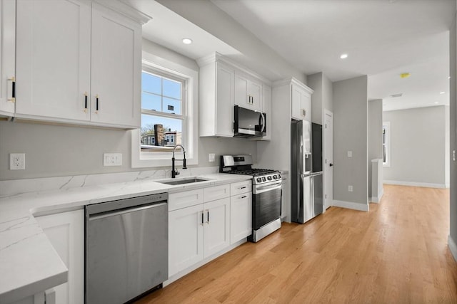 kitchen featuring sink, white cabinetry, light wood-type flooring, appliances with stainless steel finishes, and light stone countertops