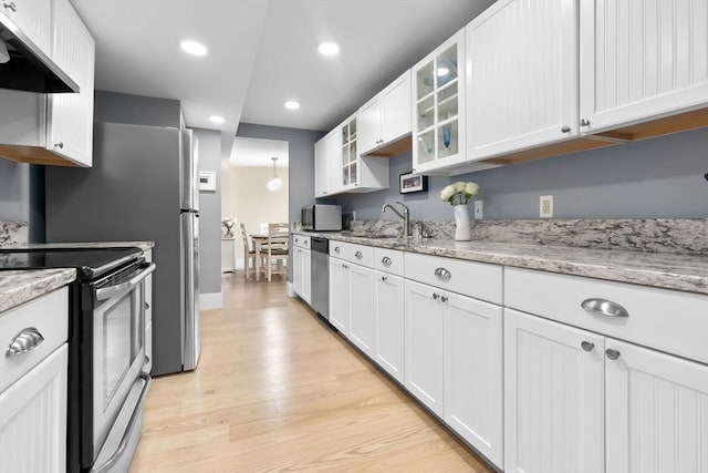 kitchen featuring stainless steel appliances, a sink, wall chimney range hood, light wood-type flooring, and recessed lighting