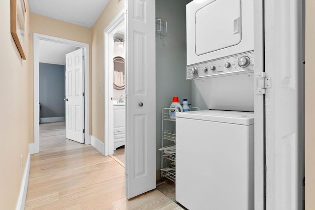 laundry area with estacked washer and dryer, light wood-style floors, and baseboards
