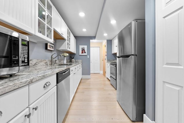 kitchen with appliances with stainless steel finishes, a sink, light wood-style flooring, recessed lighting, and white cabinets