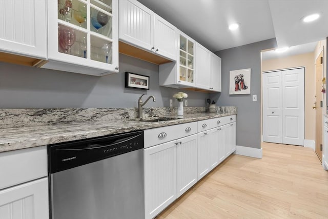 kitchen with dishwasher, a sink, white cabinets, light wood-style flooring, and baseboards