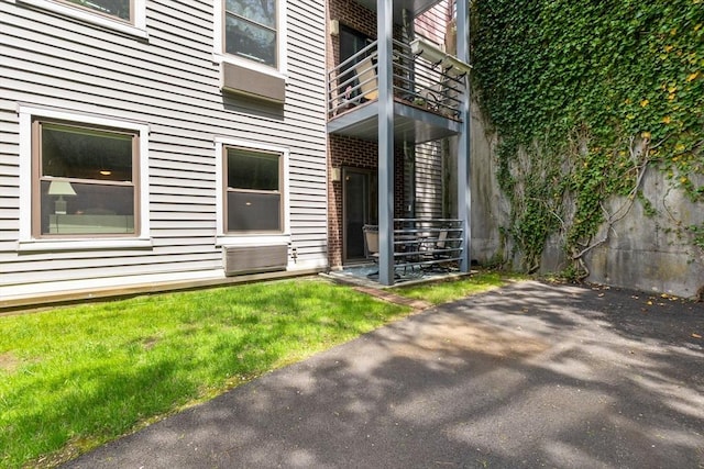 view of exterior entry with a balcony, a lawn, and a patio