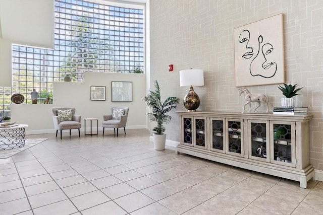 living area featuring light tile patterned flooring, baseboards, plenty of natural light, and a high ceiling