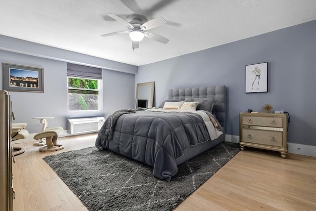 bedroom with wood finished floors, an AC wall unit, and ceiling fan