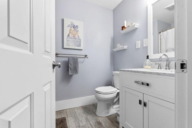 bathroom featuring baseboards, wood finished floors, toilet, and vanity