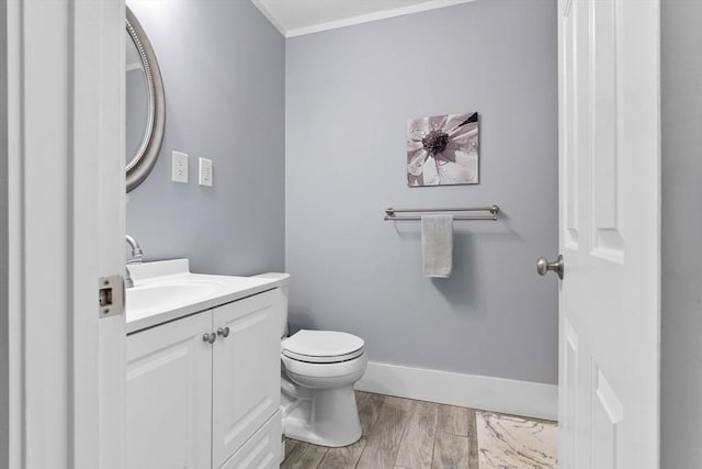half bathroom with vanity, crown molding, baseboards, toilet, and wood finished floors
