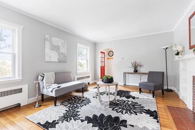 sitting room featuring light wood finished floors, arched walkways, radiator, a fireplace with flush hearth, and ornamental molding