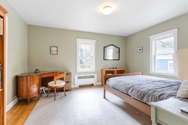 bedroom with light wood-type flooring, radiator, and multiple windows