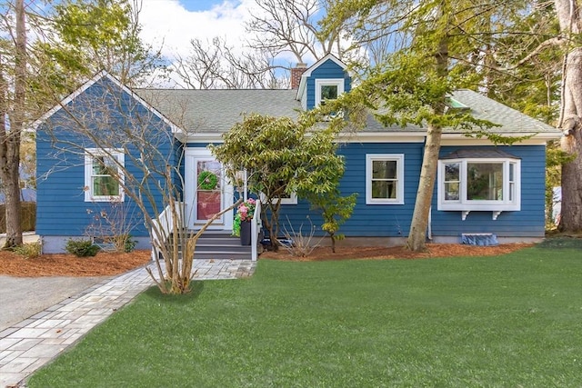 cape cod house with roof with shingles, a chimney, and a front lawn