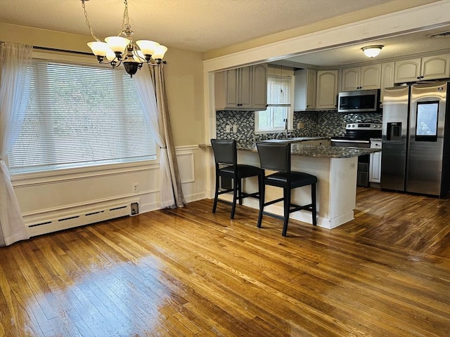 728 Stony Hill Rd, Wilbraham, MA 01095 - kitchen with stainless steel appliances, baseboard heating, a chandelier, a peninsula, and dark wood-style flooring