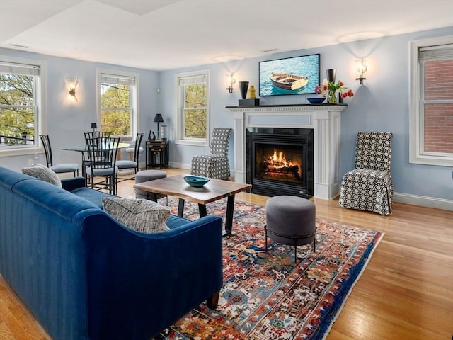living room with baseboards, wood finished floors, and a lit fireplace